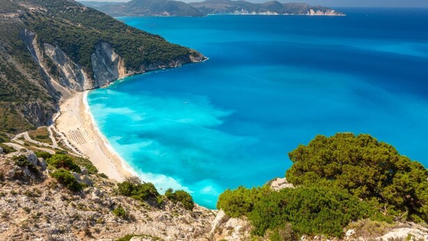 Paisaje costero con playa, aguas azul turquesa y colinas circundantes.