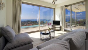 A modern living room with a large sliding glass door leading to a balcony with a pool view. - Lassi Villas Collection (Kefalonia)