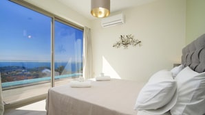 A bedroom with a large bed, a view of the sea, and a modern light fixture. - Lassi Villas Collection (Kefalonia)