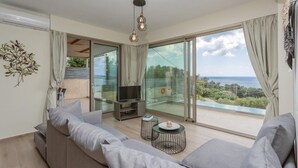 A modern living room with a sofa, TV, and a balcony with a view of the sea. - Lassi Villas Collection (Kefalonia)