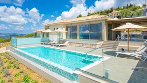 A modern villa with a swimming pool, outdoor seating, and a scenic view. - Lassi Villas Collection (Kefalonia)