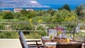 A dining table set outdoors with a view of the sea and mountains in the background. - Litsarda Villas in Apokoronos (Apokoronas)