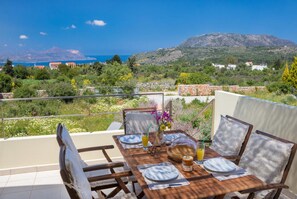 A dining table set outdoors with a scenic view of the sea and hills in the background. - Litsarda Villas in Apokoronos (Apokoronas)
