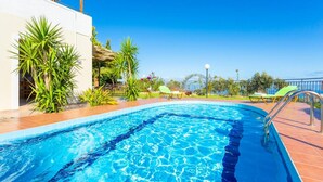 En swimmingpool med kristallklart blått vatten, omgiven av en kakelbeklädd terrass och krukväxter.