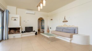 A living room with a fireplace, sofa, TV, and a small table. - Panormos Villas Collection (Mylopotamos)
