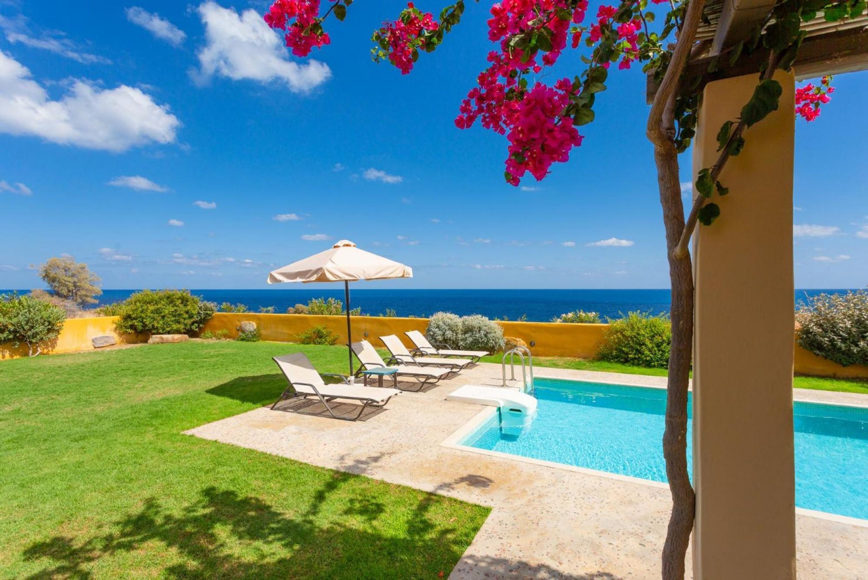 Un espace aménagé au bord de la piscine, offrant une vue dégagée sur l’océan, avec un parasol blanc et des chaises longues.