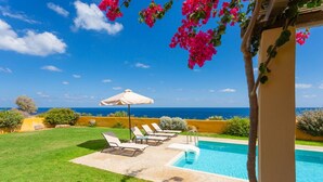 A poolside area with a clear view of the ocean, a white umbrella, and lounge chairs. - Panormos Villas Collection (Mylopotamos)