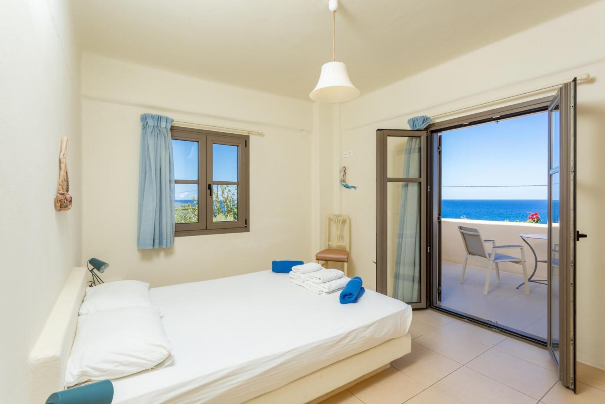 Un dormitorio con cama, una silla, una mesa y vista al mar a través de una puerta corrediza.