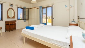 A bedroom with a bed, a dresser, a mirror, and a window with curtains. - Panormos Villas Collection (Mylopotamos)