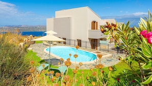 Una casa moderna de dos pisos con piscina, rodeada por un patio de piedra y abundante vegetación.