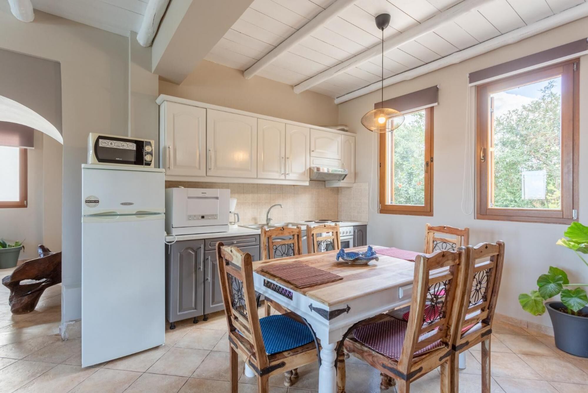 Une cuisine avec des armoires blanches, un réfrigérateur blanc, un four à micro-ondes et une cuisinière. On y trouve une table à manger avec des chaises et un luminaire suspendu.