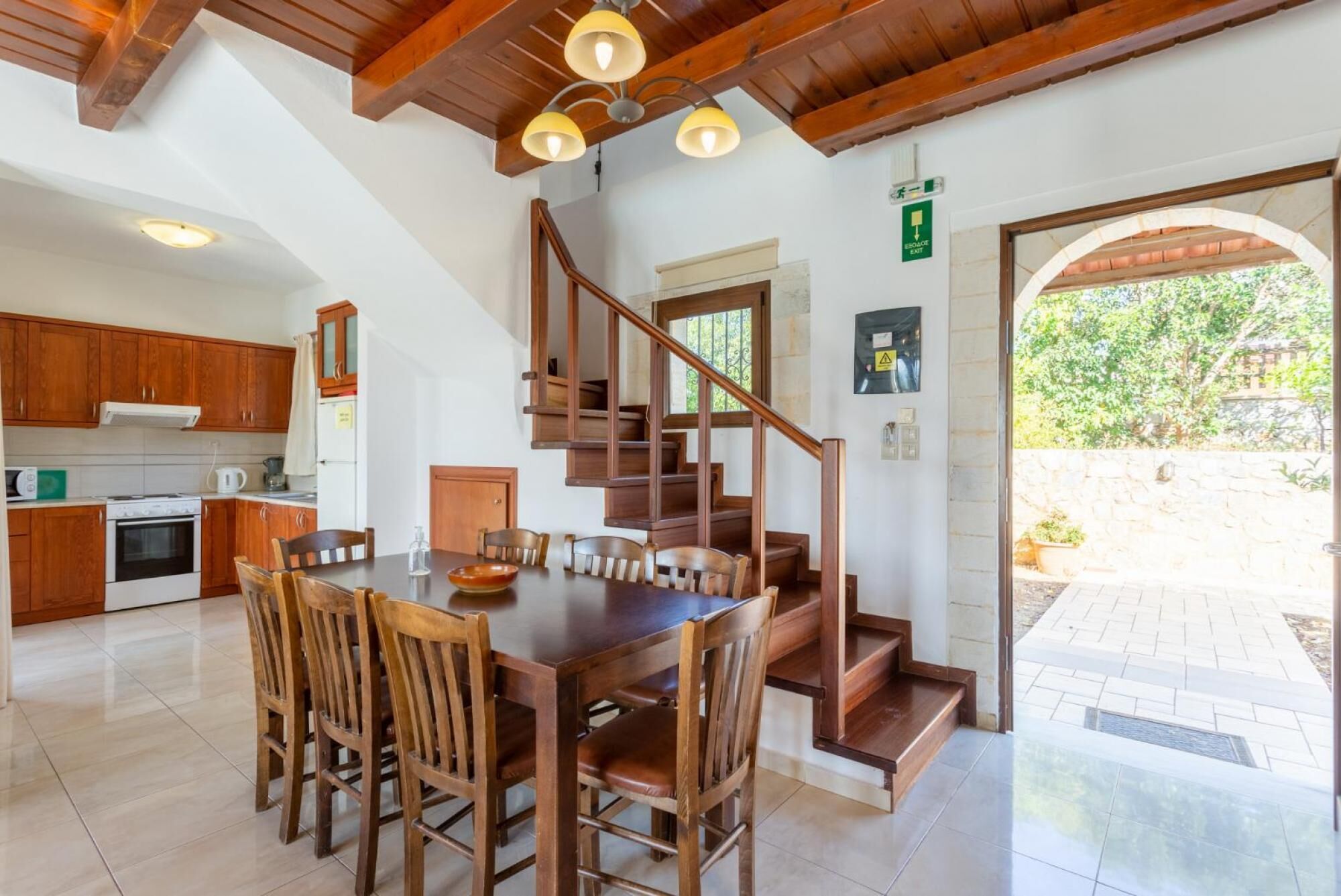 Une cuisine spacieuse avec des meubles en bois, une table à manger avec des chaises et un escalier menant à un espace extérieur.