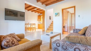 A living room with a sofa, a coffee table, and a TV. There is a staircase leading to a bathroom with a washing machine. - Spiros Villas Collection (Sfakia)