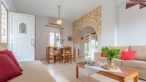 A living room with a sofa, coffee table, and a dining area with chairs and a table. - Kalyves Villas Collection (Apokoronas)