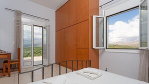 A bedroom with a bed, a wooden wardrobe, a desk with a chair, and a window with a view of the landscape. - Kalyves Villas Collection (Apokoronas)