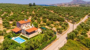 A house with a swimming pool surrounded by greenery, a road, and a distant mountain. - Kalyves Villas Collection (Apokoronas)