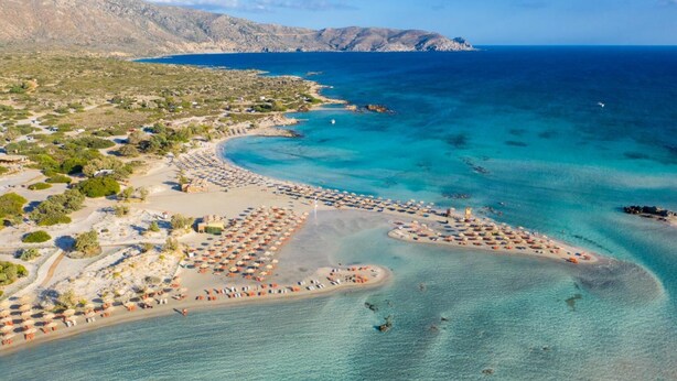 An aerial view of a coastal area with a beach, clear blue waters, and a mountainous backdrop. - Kalyves Villas Collection (Apokoronas)