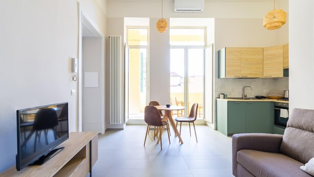 Een moderne woonkamer met een flatscreen televisie, een bank en een eethoek met stoelen.
