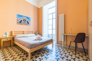 A bedroom with a bed, a desk, a chair, a radiator, and a window.