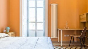 Een slaapkamer met een bed, een bureau, een stoel, een radiator en een raam.