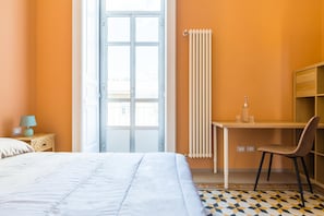 A bedroom with a bed, a desk, a chair, a radiator, and a window.