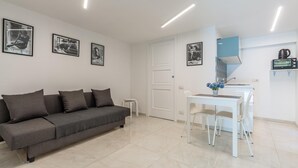 A modern living room with a grey sofa, a white dining table with chairs, and a kitchen area with a microwave and kettle. - Umberto s Nest at Toledo (Naples)