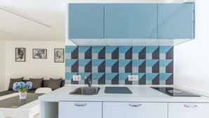 A modern kitchen with a white countertop, two sinks, and a backsplash with geometric patterns. There is a dining area with a white table and chairs, and a sofa with cushions. - Umberto s Nest at Toledo (Naples)