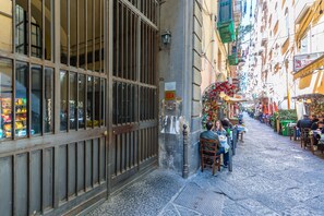 A narrow street with buildings on either side, a metal gate, and a small outdoor seating area with tables and chairs. - Umberto s Nest at Toledo (Naples)