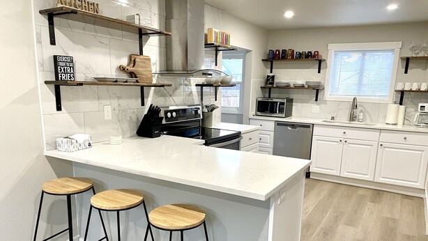 Una cocina moderna con armarios blancos, una isla central con taburetes y diversos electrodomésticos.
