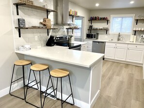 Une cuisine moderne avec des meubles blancs, un îlot central doté de tabourets et divers appareils de cuisine.