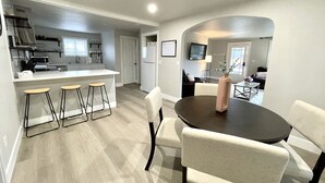 Una cocina moderna con una isla central, taburetes de bar y un comedor con mesa y sillas.