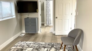 Una habitación con un televisor de pantalla plana montado en la pared, un archivador gris, una silla gris y una alfombra estampada en el suelo.
