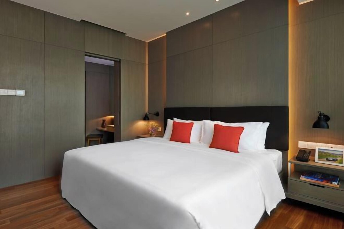 Een moderne hotelkamer met een groot bed, houten vloer en een nachtkastje met een lamp en een boek.