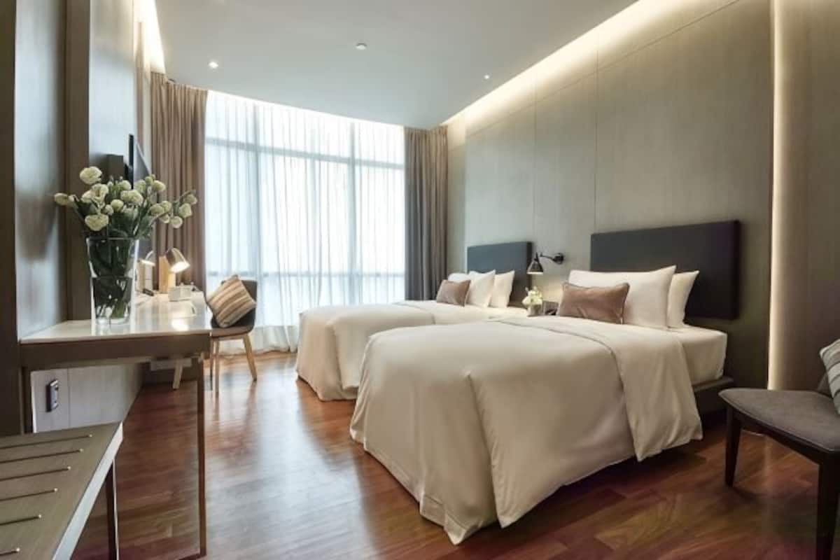 A hotel room with two beds, a desk, a chair, and a large window.