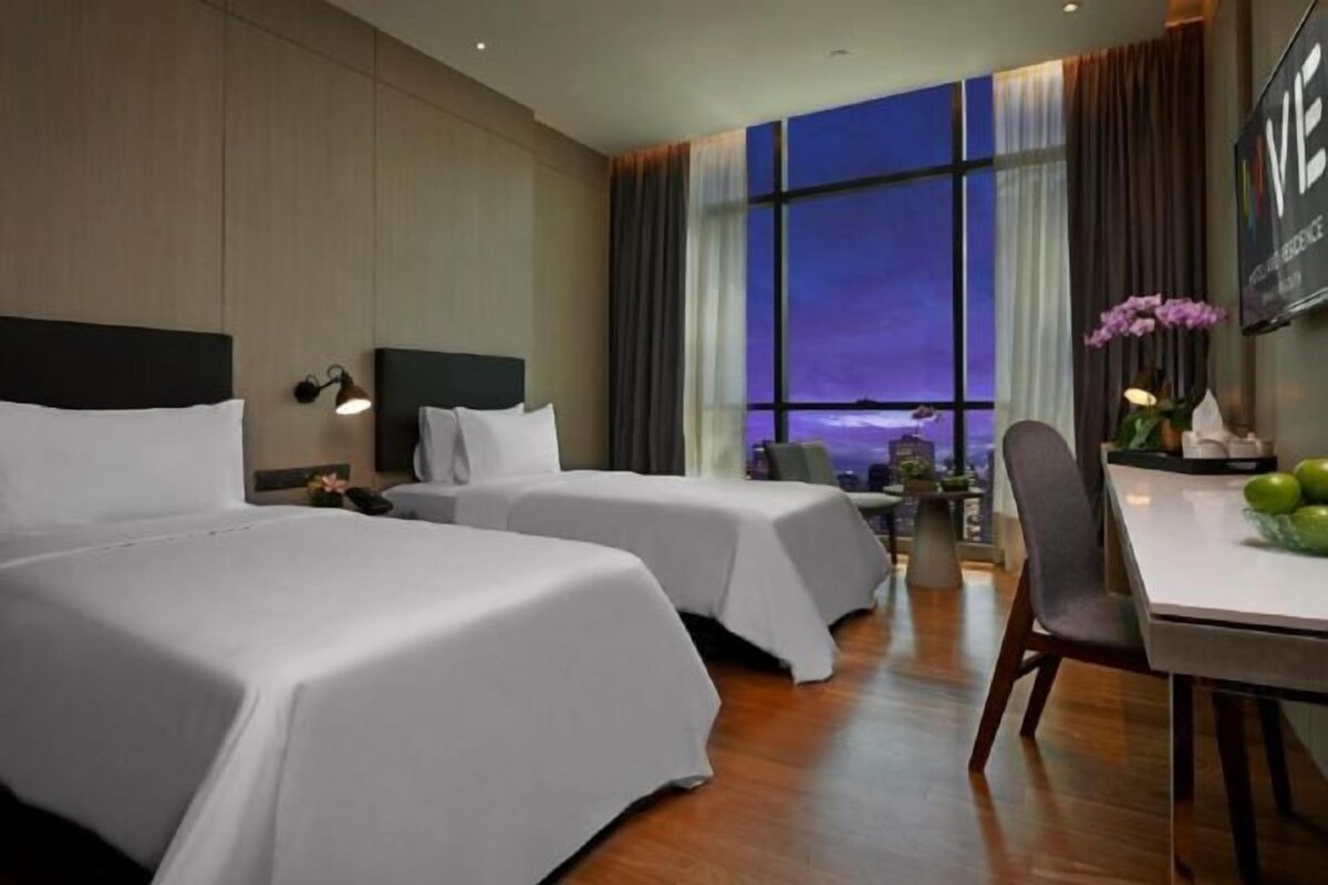 Ett hotellrum med två sängar, ett skrivbord och utsikt över kvällshimlen genom stora fönster.