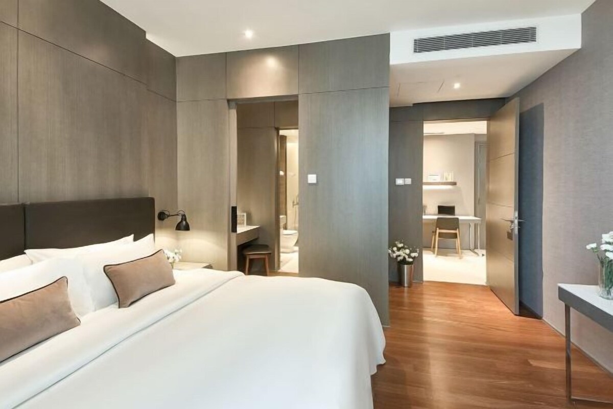 A modern hotel room with a large bed, a desk, and a bathroom visible through an open door.