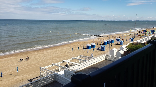 A beach with a wooden boardwalk, umbrellas, and beach huts.