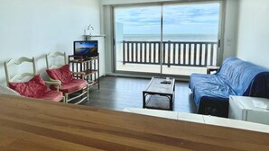 A living room with a view of the sea, a sofa, a TV, and a table.