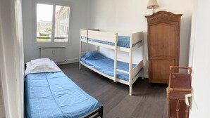 A bedroom with two bunk beds, a wooden wardrobe, and a window with a view of buildings.