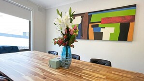 Une salle de conférence avec une table en bois, un vase rempli de fleurs et un tableau abstrait aux couleurs vives accroché au mur.