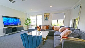 Un salon moderne avec un téléviseur à écran plat, un canapé agrémenté de plusieurs coussins, un fauteuil bleu et une table basse.