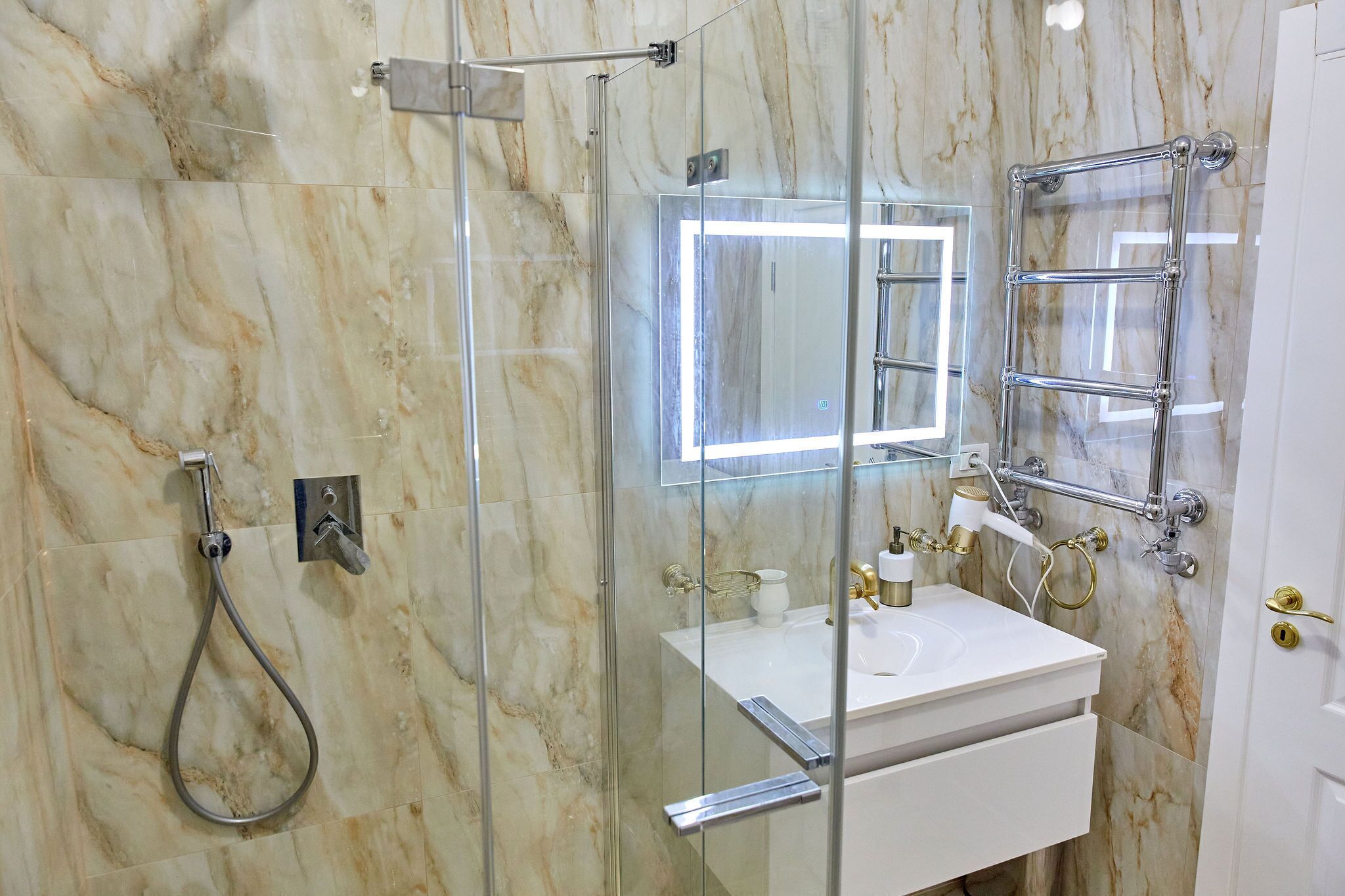 A modern bathroom with a glass-enclosed shower, a white sink, and a mirror with a chrome frame.