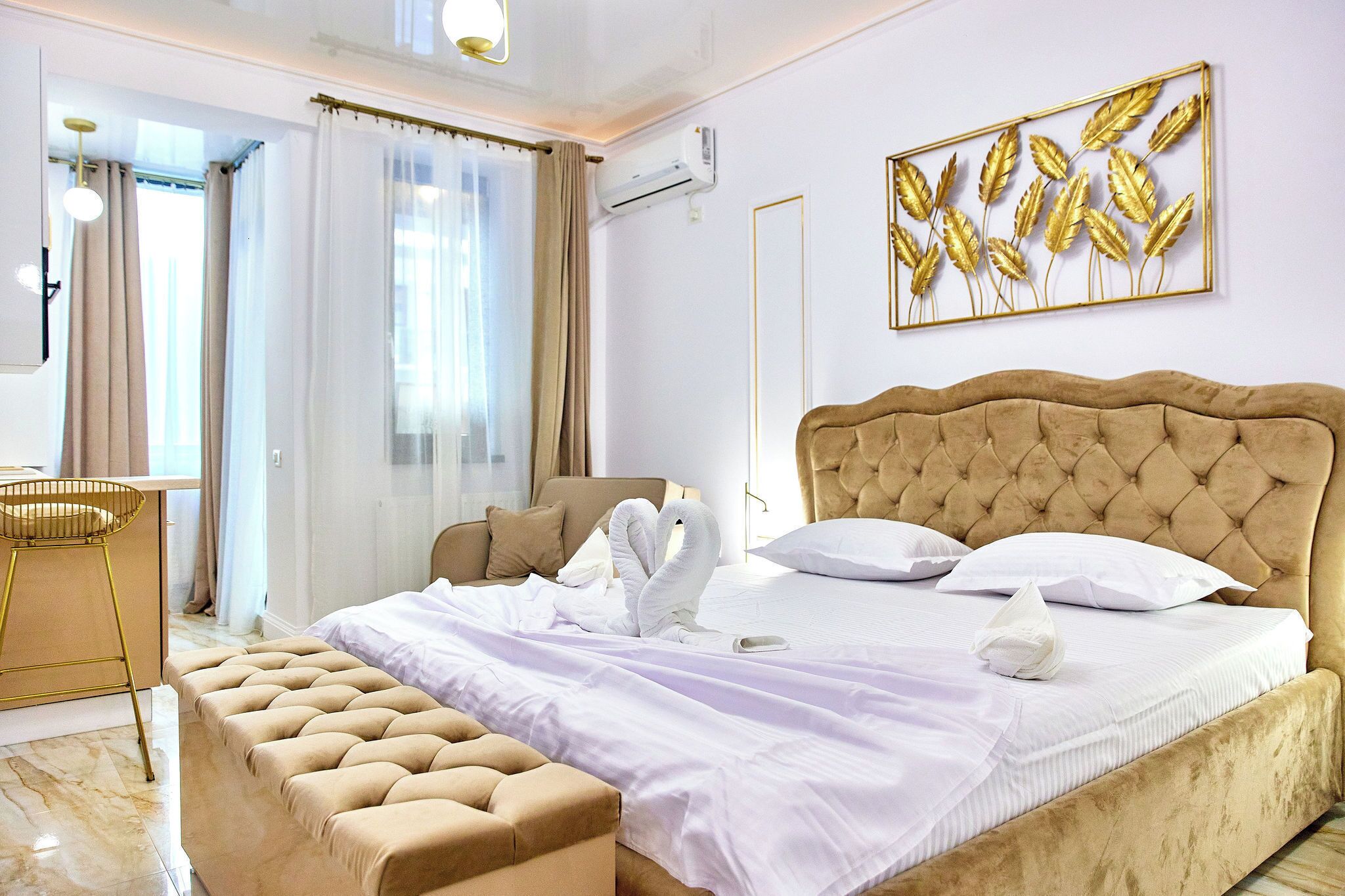 A hotel room with a large bed, a bench, a desk, and a view of the outdoors.