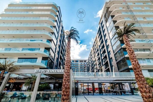 A modern hotel with a prominent entrance, palm trees, and a clear sky.