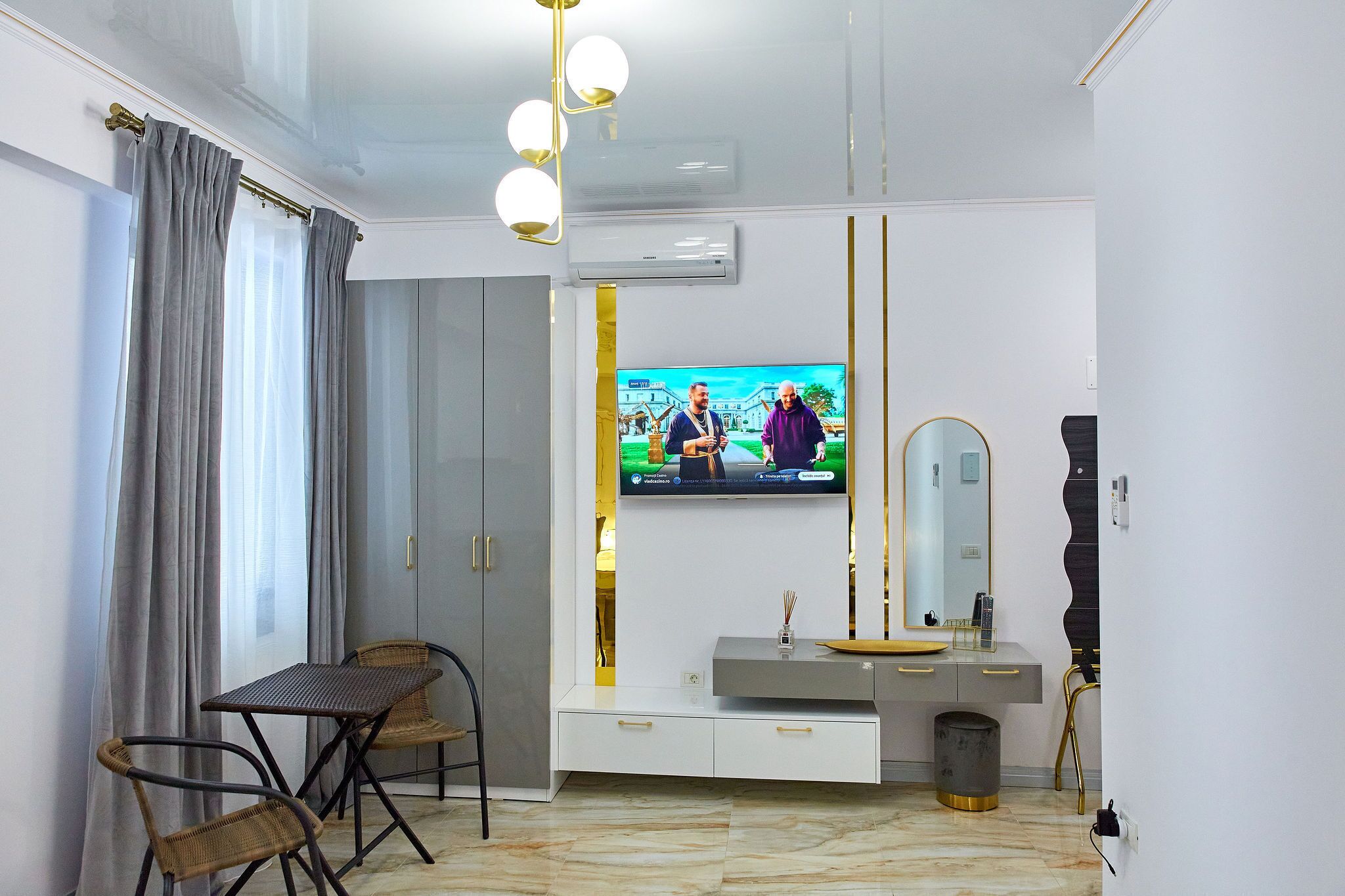 En moderne stue med et fladskærms-TV, et spisebord med stole, en sofa og et stort spejl.