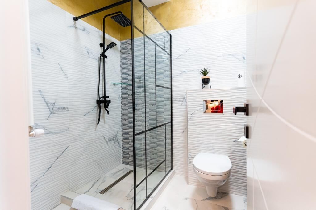 A modern bathroom with a glass-enclosed shower, a white toilet, and a marble backsplash.