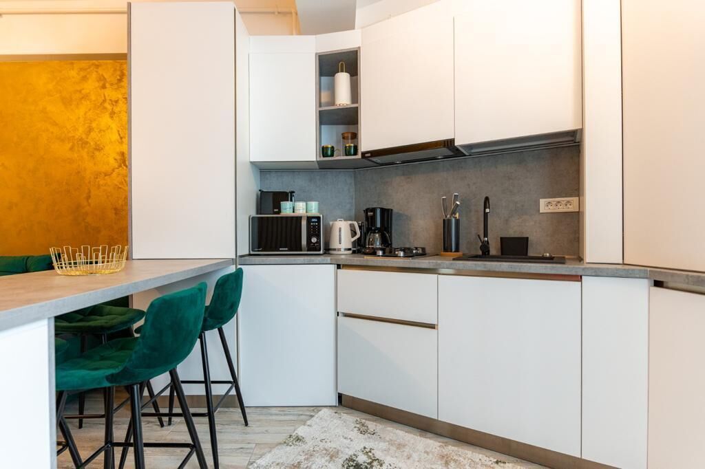 A modern kitchen with white cabinets, a grey countertop, and green chairs.