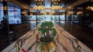 Eine moderne Lobby mit einer zentralen Pflanze im Topf, Glaswänden und einer Decke mit mehreren Kronleuchtern.