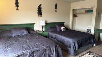A hotel room with two beds, a nightstand with a lamp, a small table with a decorative item, and a door leading to a closet.
