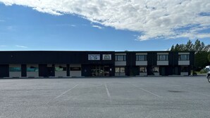 A large industrial building with multiple garage doors, a sign for Kenai Catering, and a clear sky. - The Kenai Inn (Kenai)